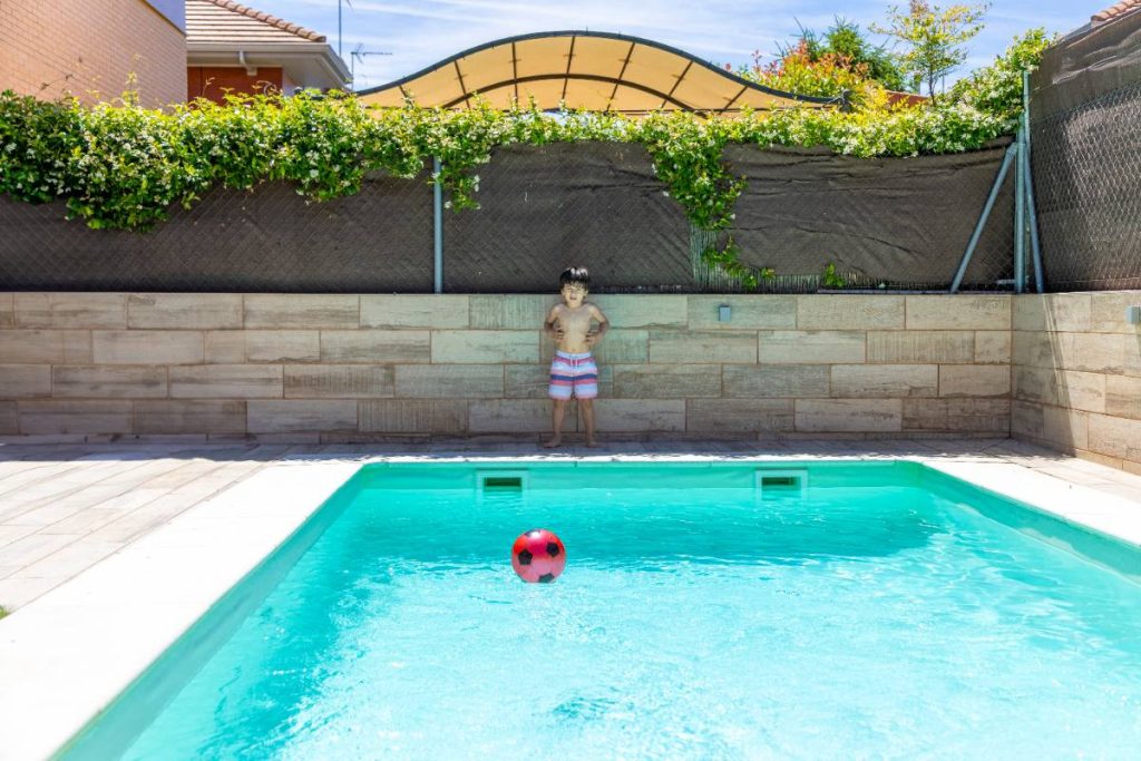 Un enfant debout au bord de la piscine devant la maison
