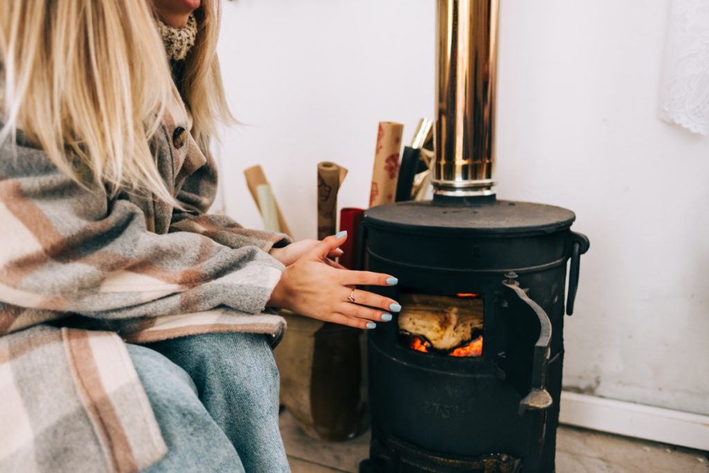 Une femme qui réchauffe sa main sur le poêle à bois