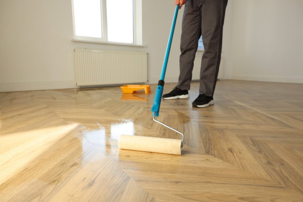 Un homme qui utilise un rouleau de peinture pour vitrifier le parquet