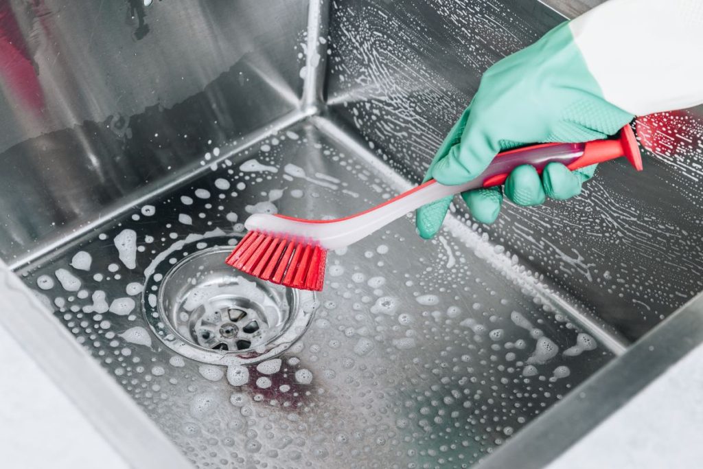 Main avec un gant et utilise une brosse pour frotter l'éveir en inox avec du savon