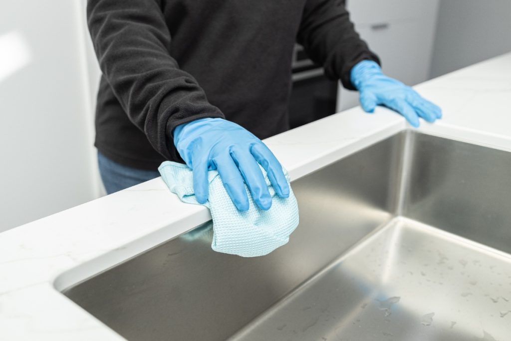 Mains avec des gants nettoyant l'évier en inox avec un chiffon