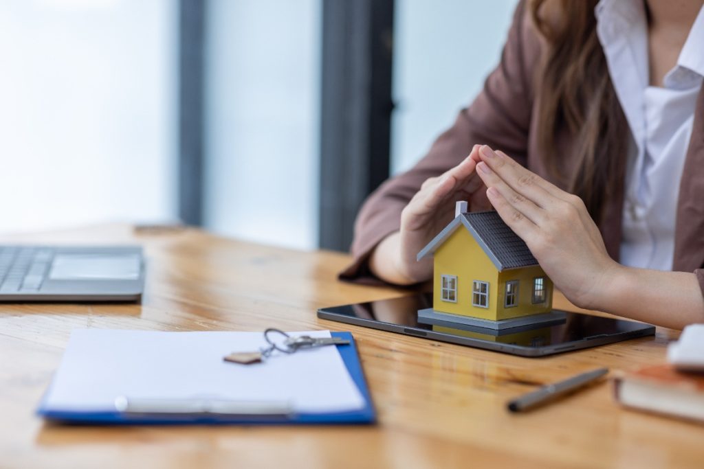 Mains posées sur une maison avec une clé et un contrat sur la table