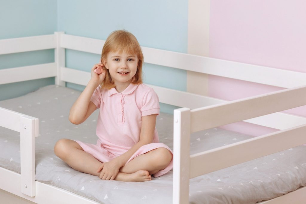 Une petite fille souriante assise sur son lit
