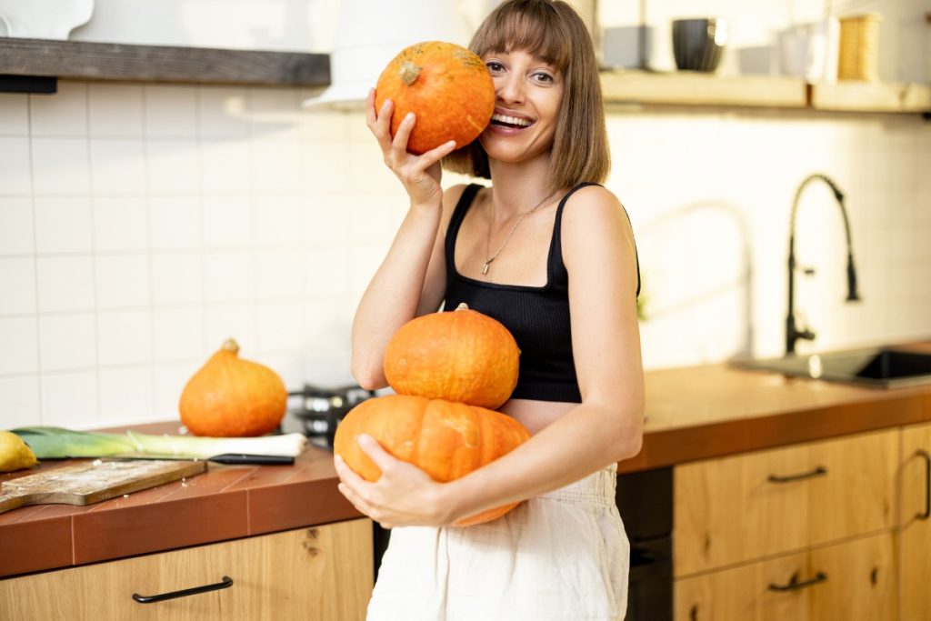 Une femme souriante tenant des potimarrons dans la cuisine