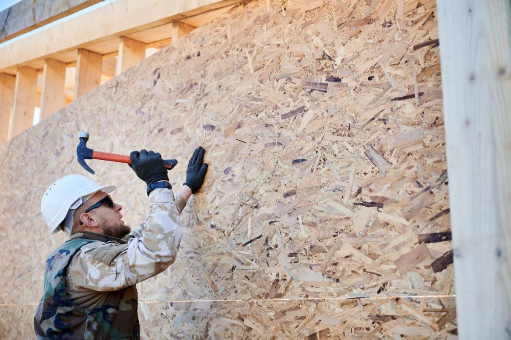 Un ouvrier clouant du panneau OSB sur une maison