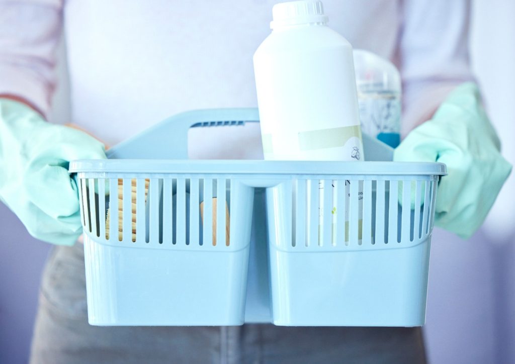 Une personne tenant un panier avec des produits de nettoyage