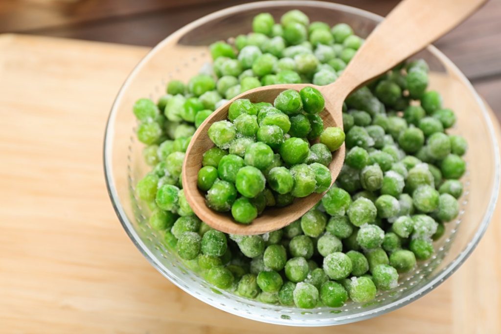 Des petits pois dans un bol en verre avec une cuillère en bois