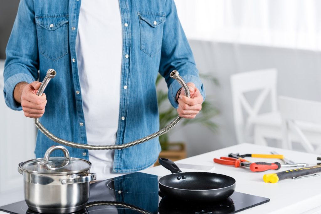 Un réparateur tenant un tuyau de plomberie dans la cuisine devant la plaque à induction