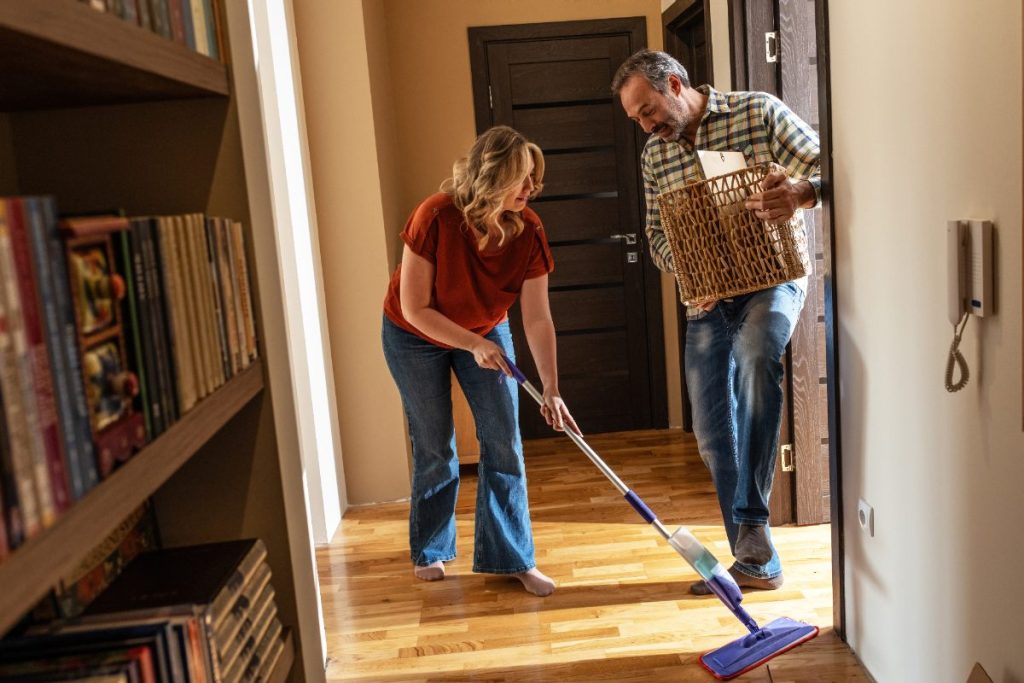 De adultes nettoyant le parquet et portant un panier lourd à l'intérieur d'une maison