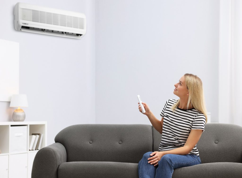 Une femme assise sur un canapé et réglant le climatiseur