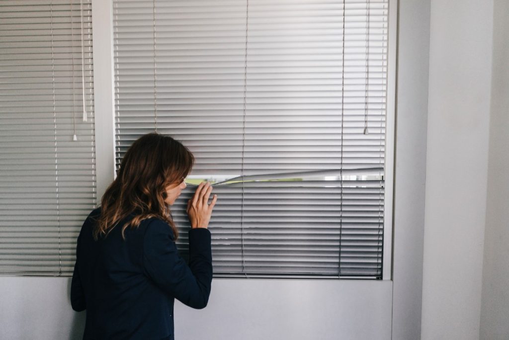 Une femme qui regadre à l'extérieur à travers le store