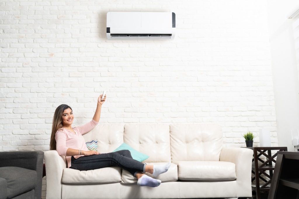 Une femme se relaxant au canapé et réglant la climatisation